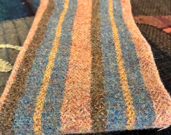 May include: A rectangular piece of thick, textured wool fabric featuring vertical stripes in shades of muted orange, dusty blue, dark brown, and golden yellow. The material has a fuzzy, felted appearance with a consistent weave throughout the pattern.