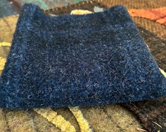 May include: A square, dark navy blue felted wool coaster with a thick, textured surface. The material displays a dense, matted fiber construction with subtle variations in blue tones throughout the square shape, showcasing a soft, fuzzy appearance.