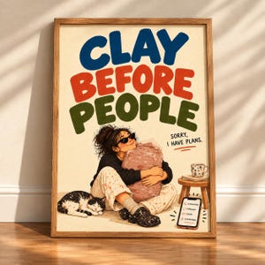 May include: A framed poster with the text CLAY BEFORE PEOPLE and SORRY, I HAVE PLANS. The illustration shows a person wearing sunglasses and paint-splattered pants hugging a large block of clay, with a cat nearby and a phone showing notifications.
