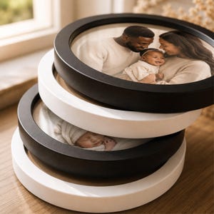May include: A stack of four circular picture frames in alternating black and white colours. The top frame displays a photograph of a family with two adults and a baby. The third frame down contains a photograph of a sleeping baby in a white hat.