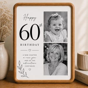 Op de afbeelding: Een rechthoekige houten lijst met een witte print met de tekst Happy 60th BIRTHDAY, A NEW CHAPTER a new you AND SO THE adventure CONTINUES. De print bevat twee zwart-witfoto's van een persoon en decoratieve lijntekeningen van bladeren.