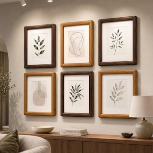 May include: A gallery wall arrangement of six rectangular framed prints featuring botanical leaf illustrations and abstract line art, displayed in alternating dark brown and light oak wood frames with white matting on a neutral wall.