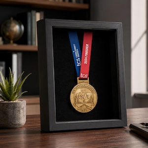 Könnte beinhalten: Eine goldfarbene TCS London Marathon 2024 Finisher-Medaille in einem schwarzen Schattenfugenrahmen. Die Medaille hängt an einem blauen und roten Band mit dem Aufdruck 2024 FINISHER und TCS. Die Medaille zeigt das Logo des London Marathons.