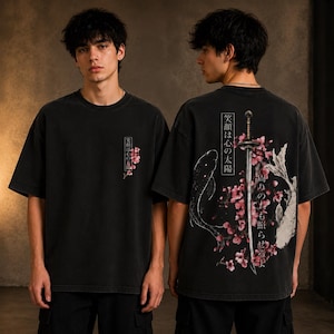 Può includere: Una t-shirt nera a maniche corte con una piccola grafica di fiori di ciliegio rosa e testo giapponese sul petto sinistro. Il retro mostra una grande spada katana, due pesci koi, fiori di ciliegio rosa e testo giapponese.