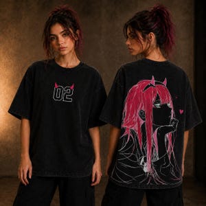 May include: A black acid-wash oversized t-shirt featuring the number 02 with small pink devil horns on the front chest. The back displays a large graphic illustration of an anime character with long pink hair, horns, and two small pink hearts.