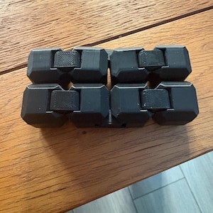 May include: A black fidget toy constructed from multiple interconnected, angular, block-like segments. The object features a series of linked, matte-finished components that form a rectangular shape, showcasing a 3D-printed texture on the surfaces.