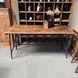 May include: A rectangular wooden table with a distressed brown finish and a dark metal folding frame. The tabletop features visible wood grain and wear, while the legs are constructed from thin, dark metal supports with a folding mechanism.