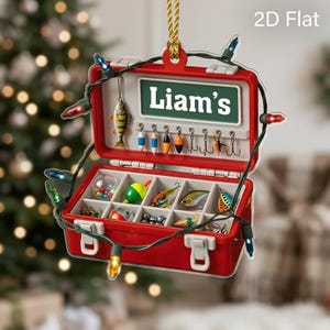 May include: A 2D flat hanging ornament shaped like an open red fishing tackle box. The interior features a green sign with the white text Liam's, hooks, and various colorful fishing lures in compartments. A string of multi-colored lights wraps around.