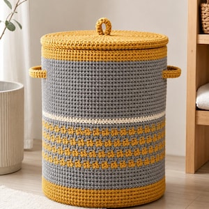 May include: A cylindrical crochet laundry basket featuring a mustard yellow lid with a central loop handle, mustard yellow base, and a grey body accented with a horizontal white stripe and a textured mustard yellow patterned band, plus two side handles.