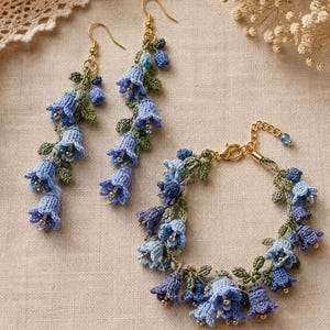 Puede incluir: Un par de pendientes colgantes y una pulsera a juego hechos de flores de ganchillo en forma de campana azul con hojas verdes y pequeñas cuentas doradas. El conjunto de joyería cuenta con ganchos de metal dorado y un cierre de mosquetón.