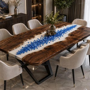 Puede incluir: Una mesa de comedor rectangular con dos tablones de madera oscura de borde natural separados por un río central de resina blanca incrustado con numerosas piedras de vidrio azul brillante. La mesa se apoya sobre una estructura de metal negro.