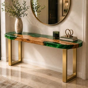May include: A console table featuring a natural wood slab with a live edge, filled with a vibrant green resin inlay. The table is supported by two rectangular gold-toned metal legs. A vase, a small glass candle holder, and books are on top.
