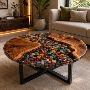 Può includere: Un tavolino rotondo con un piano in legno naturale a bordo vivo e un inserto centrale a forma di fiume riempito di pietre levigate multicolori immerse in resina trasparente, sostenuto da una base in metallo nero con gambe incrociate.