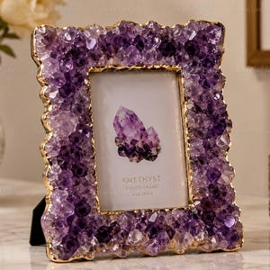 Op de afbeelding: Een rechthoekige fotolijst met een rand van dieppaarse amethistkristallen met goudkleurige randen. De centrale inzet toont een afbeelding van een amethistcluster met de tekst AMETHYST PHOTO FRAME 4x6 INCH in zwarte letters.