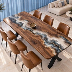 Può includere: Un tavolo da pranzo rettangolare con una superficie in venature di legno naturale e un intarsio centrale in resina fluida nei toni del blu, bianco e oro. Il tavolo è sostenuto da gambe in metallo nero ed è circondato da sei sedie in pelle marrone.