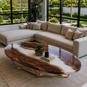 May include: An oval coffee table featuring a live-edge wood slab with a central white resin river design, supported by a geometric gold-toned metal base. The table surface holds a small potted green plant and a stack of two books.