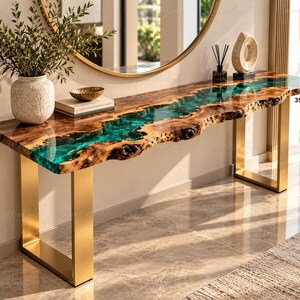 May include: A live edge wood console table with a central translucent teal resin river inlay and gold-coloured metal legs. The tabletop has a thickness of 35mm. A textured white vase with greenery, a small bowl, and a sculpture sit on top.