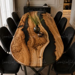 Puede incluir: Una mesa de comedor ovalada con un tablero de madera natural de borde vivo y un río de resina oscura en el centro, apoyada sobre una base de metal negro en forma de X, rodeada por ocho sillas negras tapizadas con costuras verticales.