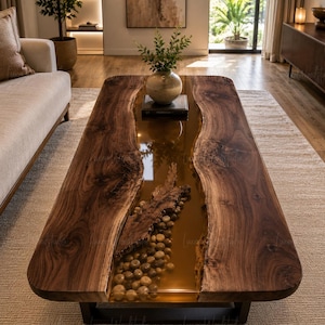 Puede incluir: Una mesa de centro rectangular con dos tablones de madera de nogal oscuro de borde natural separados por un río central de resina ámbar translúcida. La sección de resina contiene piedras de río lisas incrustadas y un trozo de madera flotante.