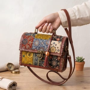 May include: A rectangular structured handbag featuring a patchwork design with various floral and geometric patterns in shades of red, yellow, blue, and black. The bag has brown leather trim, a metal latch closure, a top handle, and a long shoulder strap.