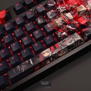 May include: A mechanical keyboard featuring black keys with red lettering and red backlighting. The spacebar and several keys on the right side display a detailed anime-style graphic print featuring characters with red eyes and dark clothing.