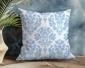 May include: A blue and white patterned throw pillow with a damask design. The pillow is sitting on a wooden floor in front of a blue wall.