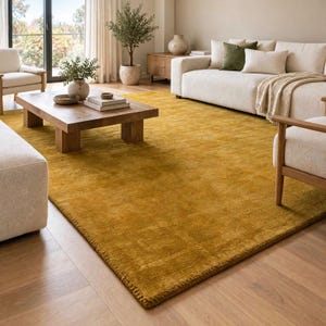 Könnte beinhalten: Ein großer, rechteckiger Teppich in einem satten, einfarbigen Senfgelb mit einer kurzen, dichten Florstruktur. Der Teppich liegt auf einem hellen Holzboden und erstreckt sich vom Vordergrund bis zur Mitte des Raumes.