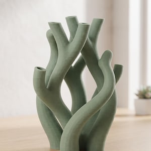 May include: A sage green candle holder with a branching, organic structure resembling coral or tree limbs. The object features multiple vertical openings at the ends of its curved, textured arms, designed to hold several candles simultaneously.