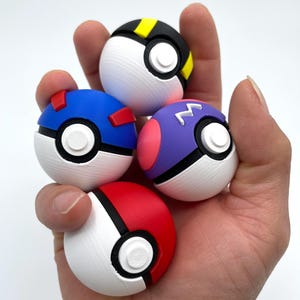 May include: Four spherical toys resembling Poké Balls in various colors. One is red and white, one is blue and white with red accents, one is black and white with yellow accents, and one is purple and white with a pink side and a white letter M symbol.