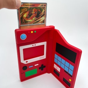 May include: A red plastic Pokedex-style case with a white screen area, blue and black buttons, and a green rectangular panel. A Charmander trading card with 60 HP is inserted into the top slot of the device, which features a hinge on the right side.
