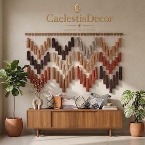 May include: A wall hanging featuring multiple rows of yarn tassels in shades of brown, tan, and rust, suspended from a wooden rod. The text CaelestisDecor and Elevate Your Space is visible above the hanging. A wooden sideboard sits below.