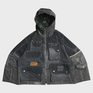 Könnte beinhalten: Eine anthrazitfarbene Kapuzenjacke aus Denim mit durchgehendem Frontreißverschluss, mehreren Utility-Taschen mit silberfarbenen Druckknöpfen, einer Sicherheitsnadel und einem dunkelgrünen Innenfutter mit weißem Blumenmuster. Der Text Crazy Guts ist auf einer Tasche aufgedruckt.
