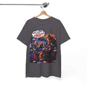 May include: A dark gray t-shirt featuring a graphic of a person sitting in a gaming chair playing a video game. A speech bubble above the person reads, "WHY PEOPLE GOTTA CHEAT!?" The design includes a computer monitor, gaming equipment, and red accents.