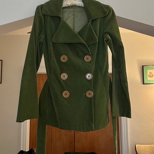May include: A green corduroy jacket with a double-breasted closure and a belt. The jacket has six large brown buttons.
