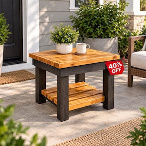 May include: A square wooden side table featuring a natural light brown slatted top and lower shelf supported by four thick, dark charcoal-colored legs. A white ceramic mug and a small potted green plant sit on the surface, which has a red tag reading 40% OFF.