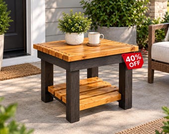May include: A square wooden side table featuring a natural light brown slatted top and lower shelf supported by four thick, dark charcoal-colored legs. A white ceramic mug and a small potted green plant sit on the surface, which has a red tag reading 40% OFF.