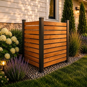 May include: A square outdoor privacy screen featuring horizontal natural wood slats framed by four sturdy black metal posts. The structure is designed to enclose equipment, standing on a bed of small grey stones in a garden setting.