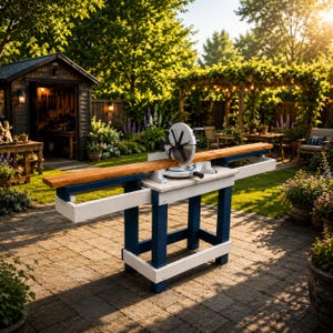 May include: A white and navy blue miter saw stand with an integrated miter saw and a long wooden board positioned on the cutting surface. The stand features a sturdy rectangular frame with horizontal support rails and a flat top work surface.