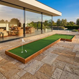 Puede incluir: Un putting green exterior en forma de L con marco de madera, que cuenta con césped artificial verde, tres pelotas de golf blancas y tres banderas blancas en mástiles. El putting green está situado en un patio de piedra frente a una casa moderna.