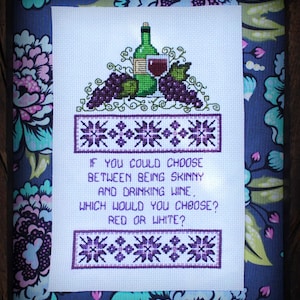 Peut inclure: Broderie au point de croix encadrée dans du bois. Le motif représente une bouteille de vin verte, un verre de vin rouge et des grappes de raisin violet. Le texte dit : « Si vous pouviez choisir entre être mince et boire du vin, lequel choisiriez-vous ? Rouge ou blanc ? »