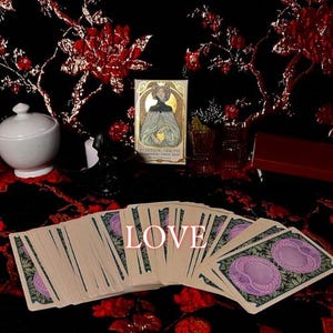 May include: A deck of tarot cards with a fan-shaped spread featuring purple circular motifs on the back, positioned in front of a box labeled Ethereal Visions Illuminated Tarot Deck by Matt Hughes, with the word LOVE overlaid in white text.