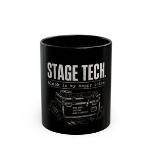 May include: A black ceramic mug featuring the white text STAGE TECH. and black is my happy colour. Below the text is a detailed illustration of a road case with cables and equipment, including the text WORK HARD. STAY LOW. MAKE IT LOOK EASY.