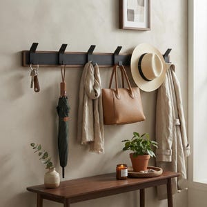 Pode incluir: Um cabide de parede com base de madeira escura e seis ganchos de metal preto fosco. O cabide sustenta um conjunto de chaves, um guarda-chuva verde-escuro, um cachecol bege, uma bolsa de couro castanha, um chapéu de palha e um sobretudo bege.