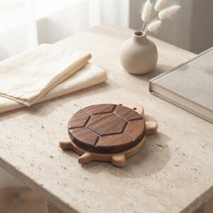 Peut inclure: Un objet en bois en forme de tortue avec une carapace en noyer brun foncé ornée de motifs hexagonaux sculptés et une base en bois plus clair. La tortue présente une finition lisse, une tête arrondie avec deux petits yeux sombres.