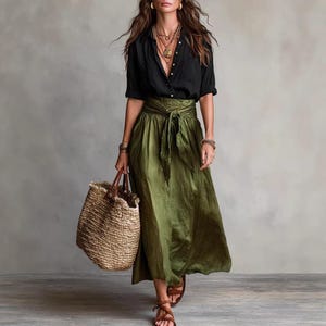 May include: A black button-down shirt with long sleeves and a collar, paired with a long olive green skirt featuring a tie-waist detail. The outfit includes a large woven straw tote bag, layered gold necklaces, and brown strappy sandals.