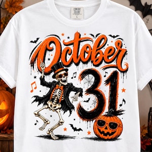 May include: A white t-shirt featuring a graphic of a dancing skeleton wearing a top hat, orange bowtie, and sunglasses. The text reads October 31 in large orange and black lettering. A jack-o'-lantern wearing sunglasses sits below the text.