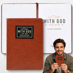 Può includere: Un libro di devozioni dalla texture in pelle marrone intitolato One Minute With God For Men 365 Daily Devotions. La copertina presenta un'etichetta rettangolare nera con testo dorato. Il libro è mostrato sia chiuso che aperto, con il titolo.