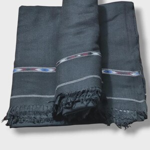 May include: A black rectangular scarf featuring a woven texture and fringed edges. The fabric is adorned with horizontal stripes in white, red, and blue, creating a repeating pattern across the surface. The scarf is folded to display its details.