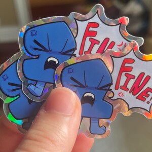 May include: A holographic sticker featuring a blue, anthropomorphic character with an angry expression and a speech bubble containing the red text "FINE!". The character has a furrowed brow, clenched teeth, and small limbs, with a star-like symbol.