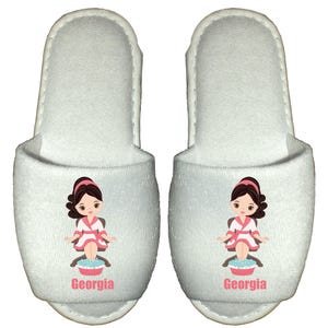 May include: White spa slippers with a cartoon illustration of a woman getting a pedicure. The slippers have the name "Georgia" printed on them.